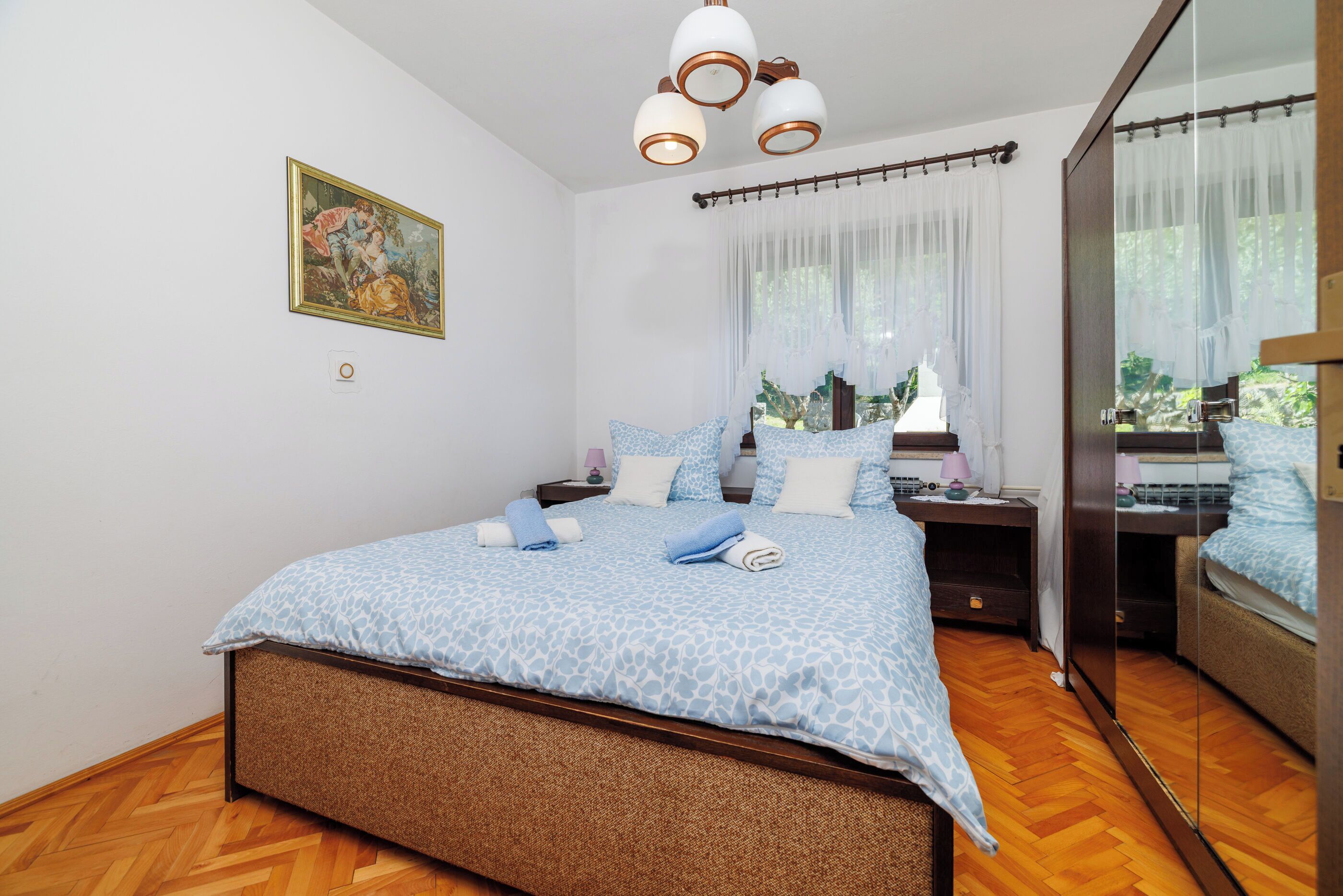 A bedroom with a bed, bedside tables, a mirror, and a window with sheer curtains.