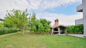A grassy outdoor area with a stone-built barbecue area and a brick chimney. - Apartment Sanja (Rab)