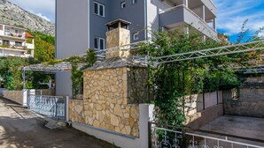 A multi-story residential building with balconies, a stone wall, and a metal fence. - Apartment Anica (Omis)