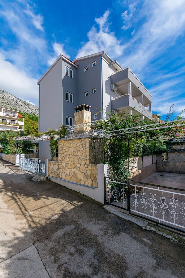 A multi-story residential building with balconies, a stone wall, and a metal fence.