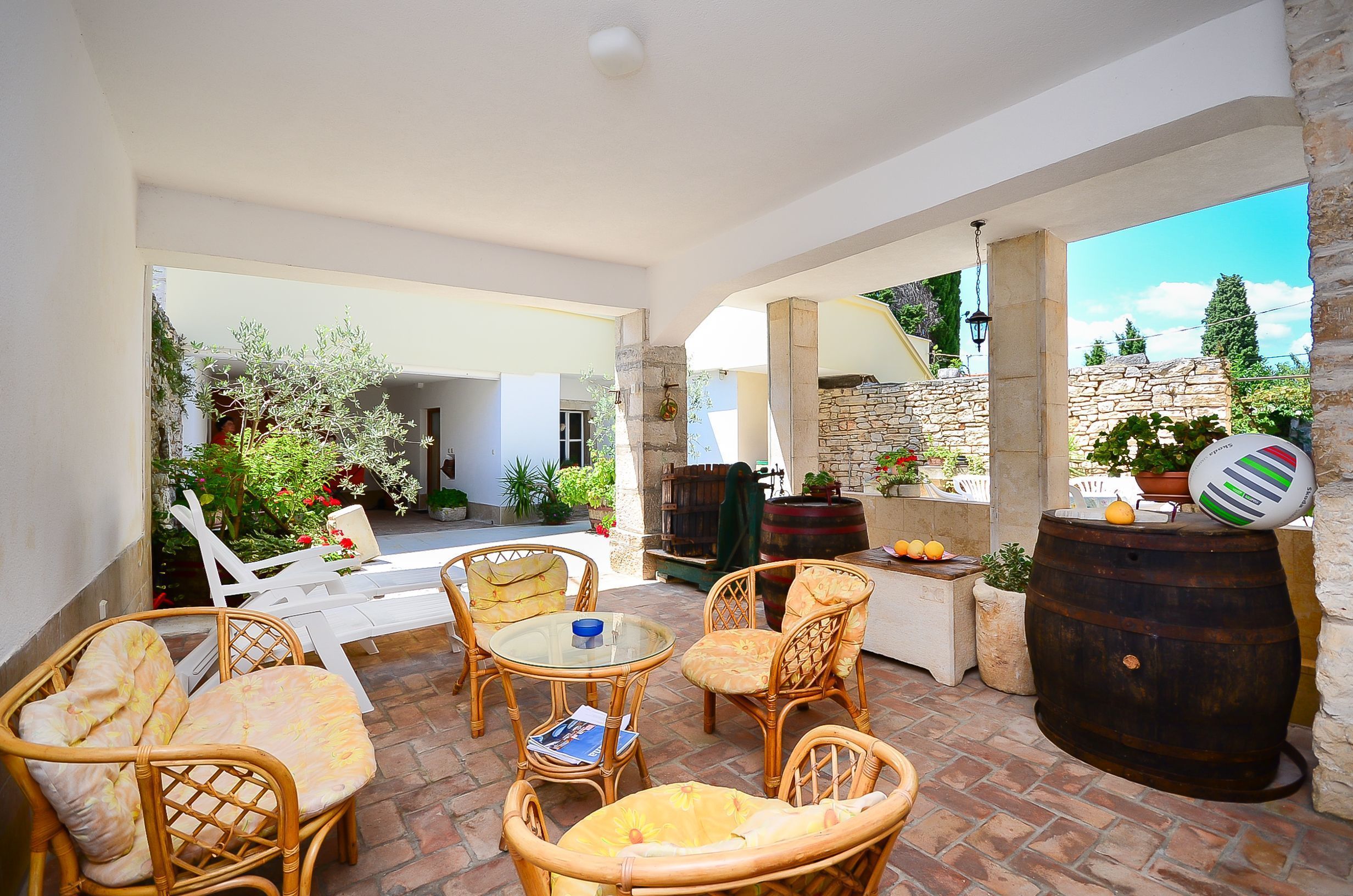 An outdoor patio with wicker furniture, a stone barrel, and potted plants.