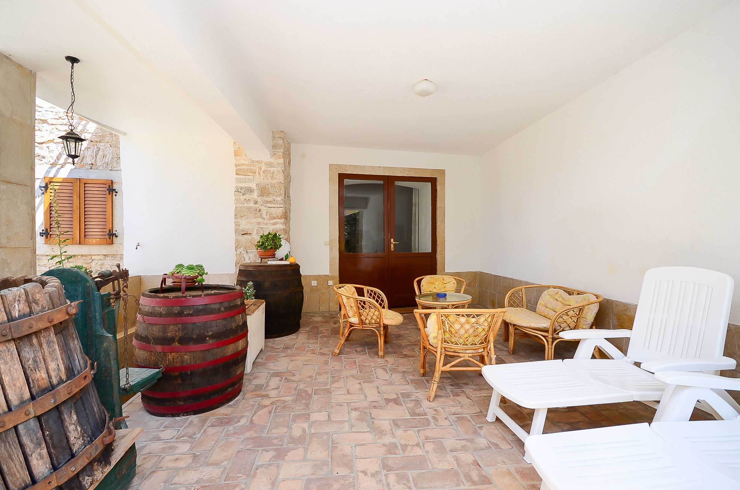 Eine Terrasse mit Korbmöbeln, einem Holzfass und einer Tür zu einem Innenbereich.