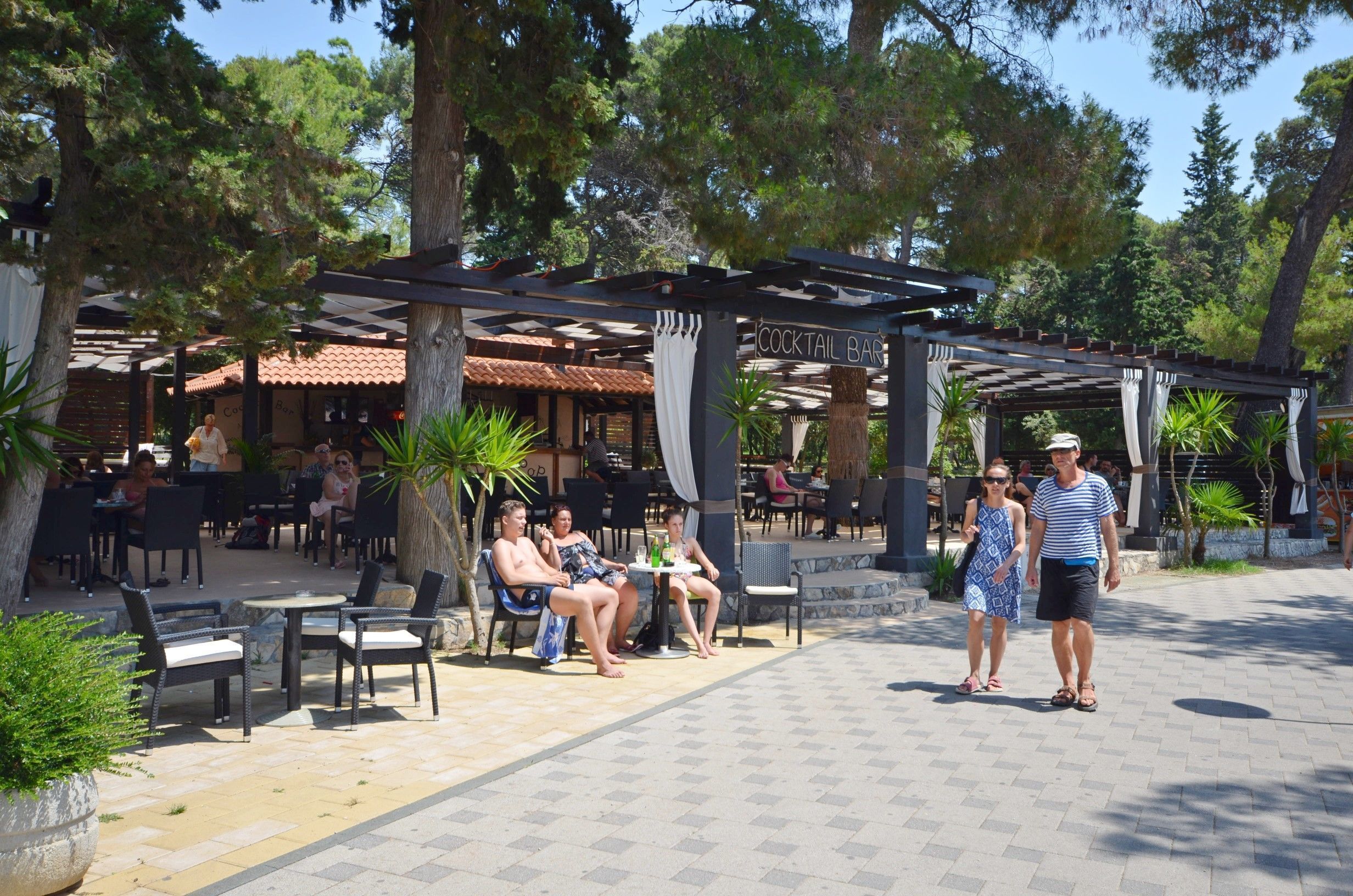 Een terras met tafels en stoelen, een overdekte bar en een pergola.