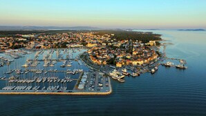 Vista aèria d'una població costanera amb un port de vaixells, envoltada d'edificis residencials i una gran massa d'aigua.