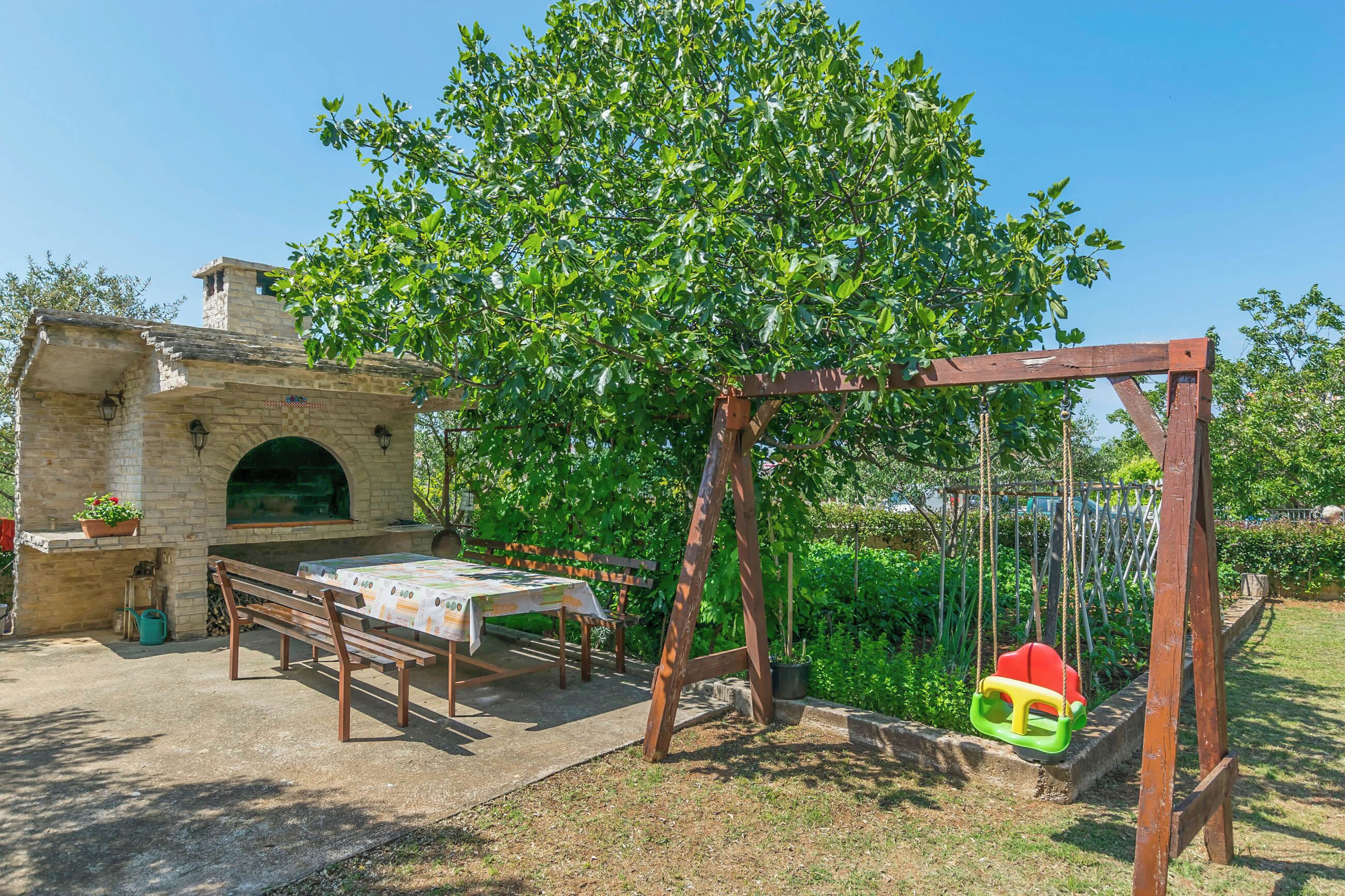 A patio with a table and benches, a swing set, and a stone building with an arched window.