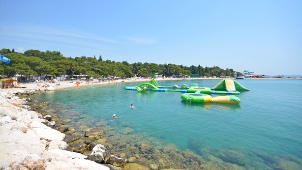 Platja amb aigua cristal·lina, roques i jocs inflables.