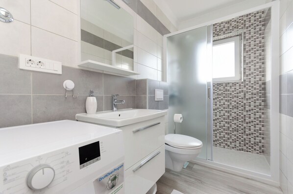 A modern bathroom with a shower, toilet, and a built-in washing machine. - Apartments Nada (Rab)