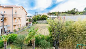 Un quartiere residenziale con un cortile pavimentato, circondato da case con tetti in tegole rosse e un fitto siepe sempreverde in primo piano.