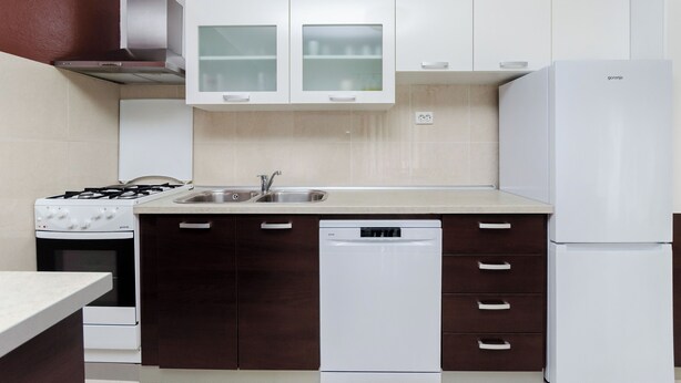 Una cucina moderna con mobili bianchi, una cappa aspirante in acciaio inossidabile, una lavastoviglie e un frigorifero.