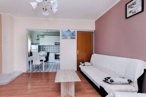 A living room with a sofa, a coffee table, and a dining area visible through an open door. - Apartments Nada (Rab)