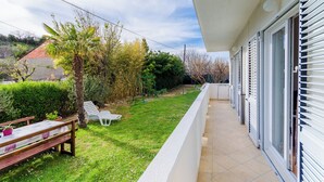 Un balcone con ringhiera bianca, un piccolo tavolo e una sedia, e una palma.