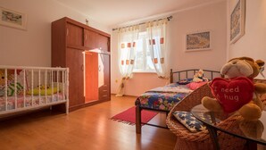 Ein gemütliches Schlafzimmer mit einem Babybett, einem Bett mit Blumenmuster und einem Korbstuhl, sowie einem Stofftier.