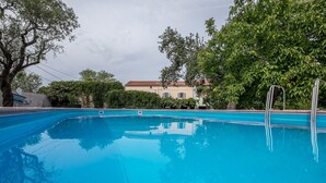 A swimming pool with clear blue water, surrounded by trees and a building in the background.