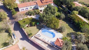 An aerial view of a residential property with a swimming pool, surrounded by greenery and a paved driveway.