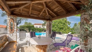 Ein Terrassenbereich im Freien mit Steinsäulen, Holzboden, einem Steintisch und Lounge-Stühlen.