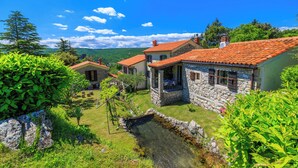 Una casa in pietra con tetto in tegole rosse, un piccolo giardino e un ruscello cristallino.