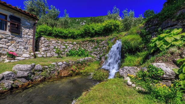 Una casa in pietra con una piccola cascata e un ruscello.