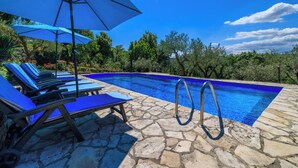 Una piscina con piastrelle in pietra, poltrone da relax blu e ombrelloni.