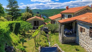 Una casa in pietra con tetto in tegole rosse, un piccolo giardino e vista su una collina.
