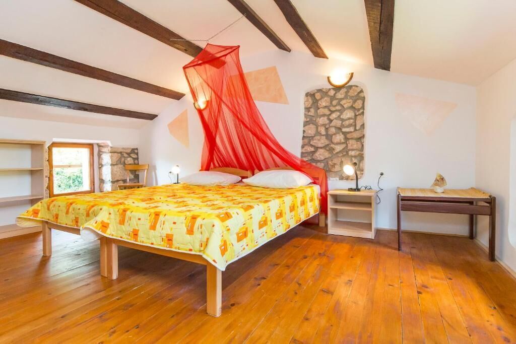 Un dormitorio con cama, mesita de noche, banco de madera y pared de piedra.