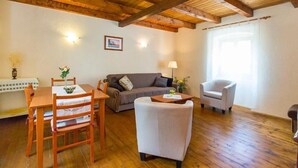 A cozy living room with a wooden ceiling, a sofa, a dining table with chairs, and a small armchair. - House Dean (Labin)