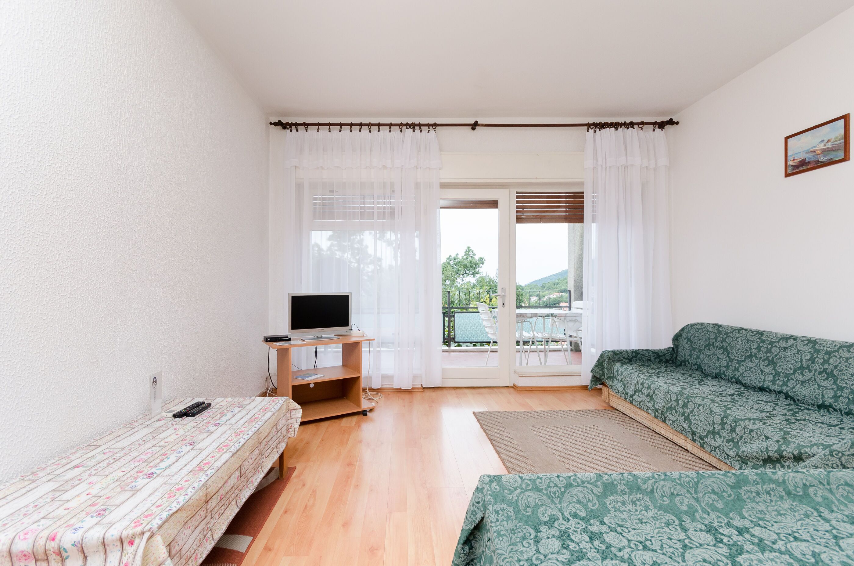 A room with a bed, a desk with a TV, a sofa, and a view through a door.