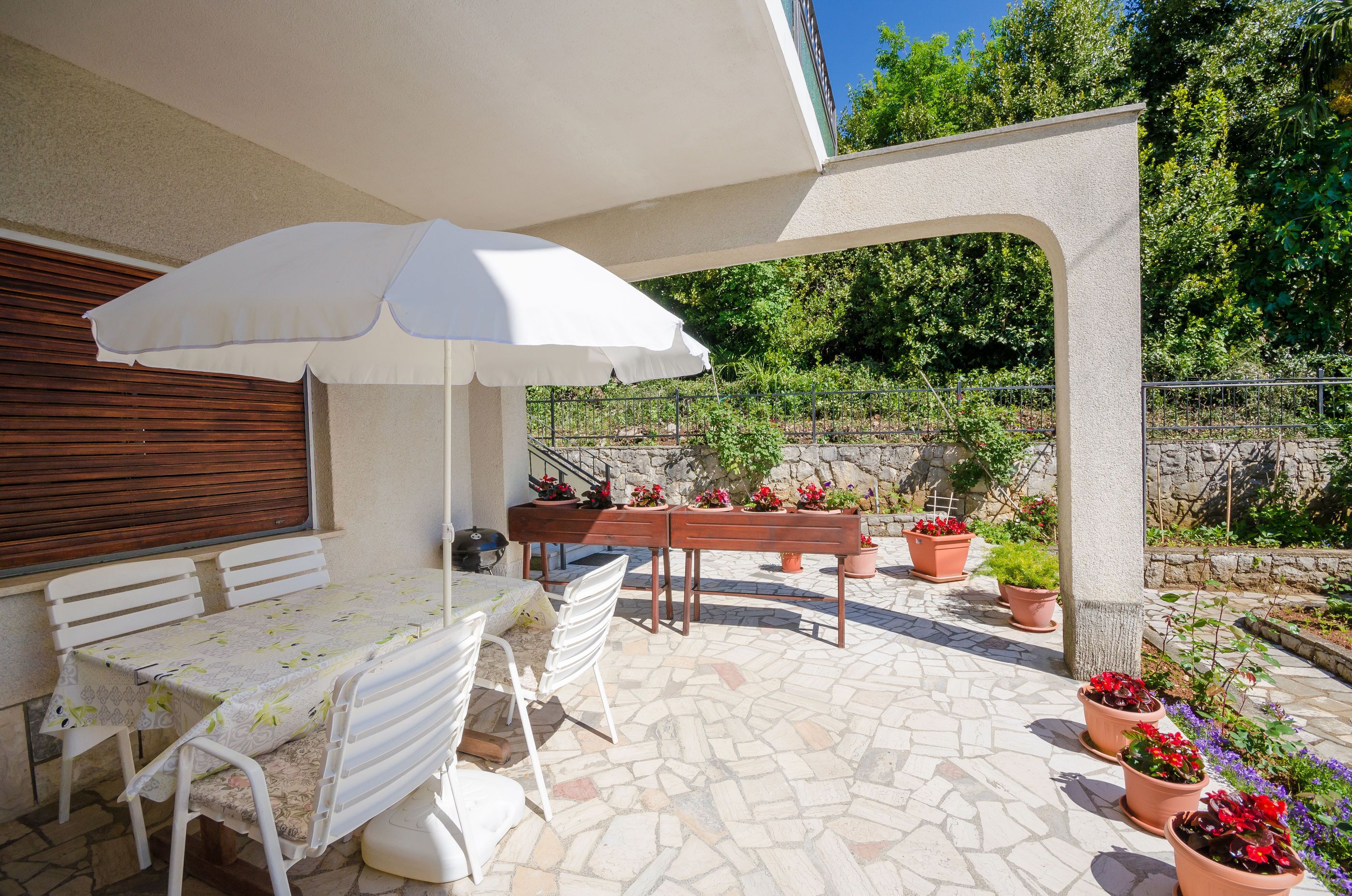 An outdoor patio with a table and chairs, surrounded by potted plants and a stone floor.