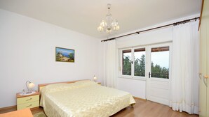 Un dormitorio con cama, mesita de noche, lámpara, ventana con cortinas y un cuadro en la pared.