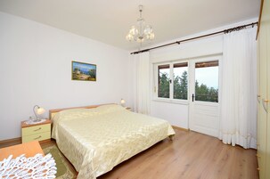 Un dormitorio con cama, mesita de noche, lámpara, ventana con cortinas y un cuadro en la pared.