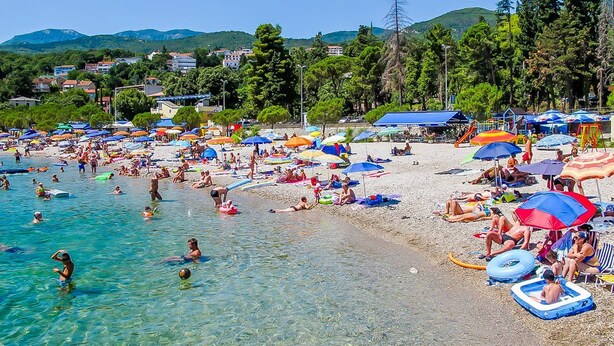 Una playa concurrida, con agua cristalina, sombrillas y gente nadando.