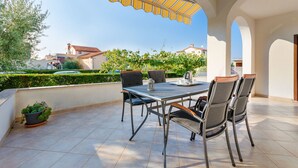 An outdoor patio with a table and chairs, a striped awning, and a potted plant. - Apartment Marija (Porec)