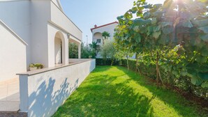 A well-maintained garden with a white building featuring arched windows and a red-tiled roof. - Apartment Marija (Porec)
