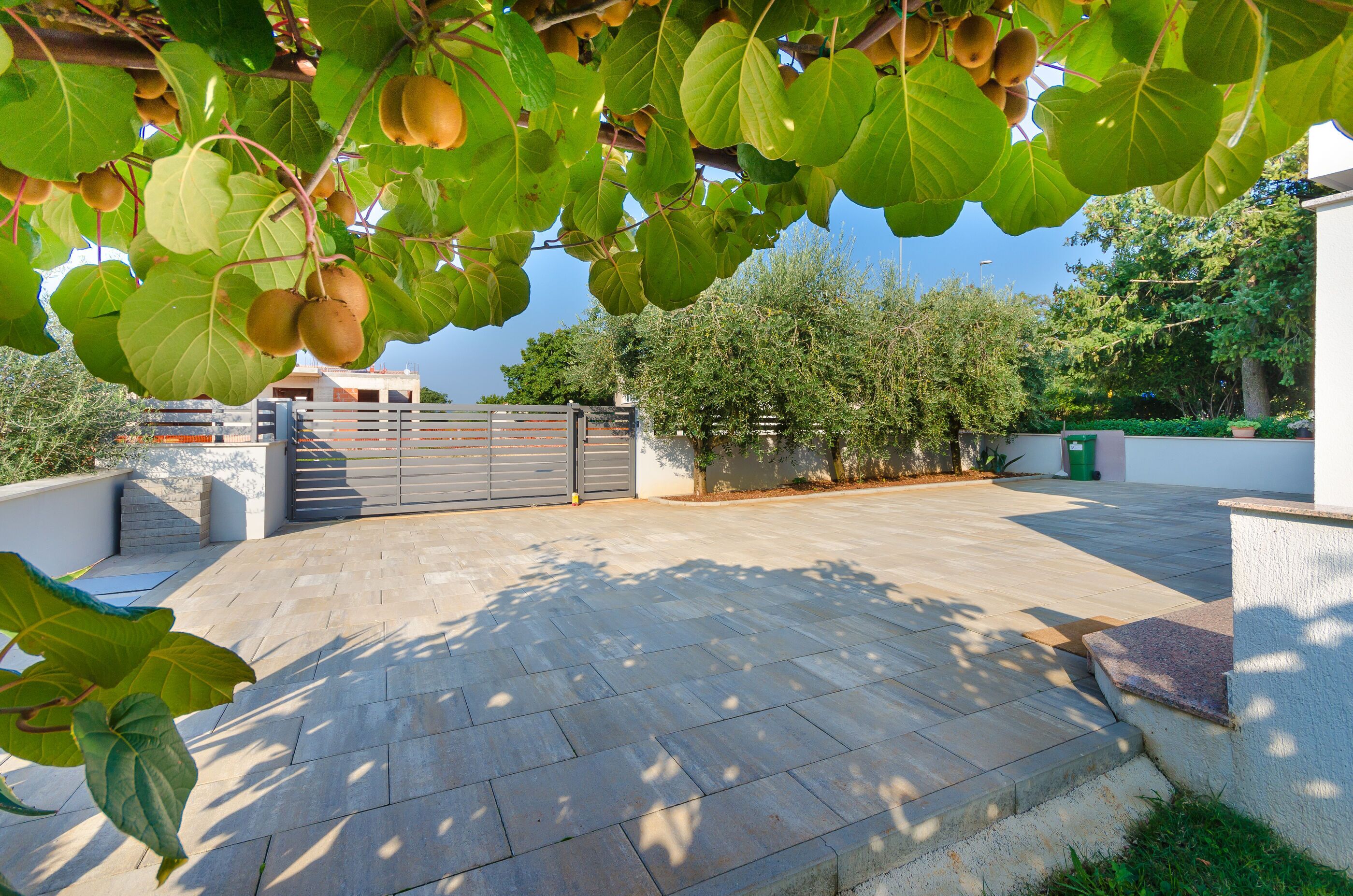A paved outdoor area with a gate, greenery, and a building in the background.