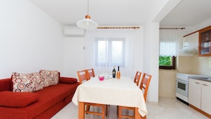 A dining area with a table set for two, a red sofa with patterned cushions, and a kitchen with a stove and cabinets. - Apartment Marija (Porec)