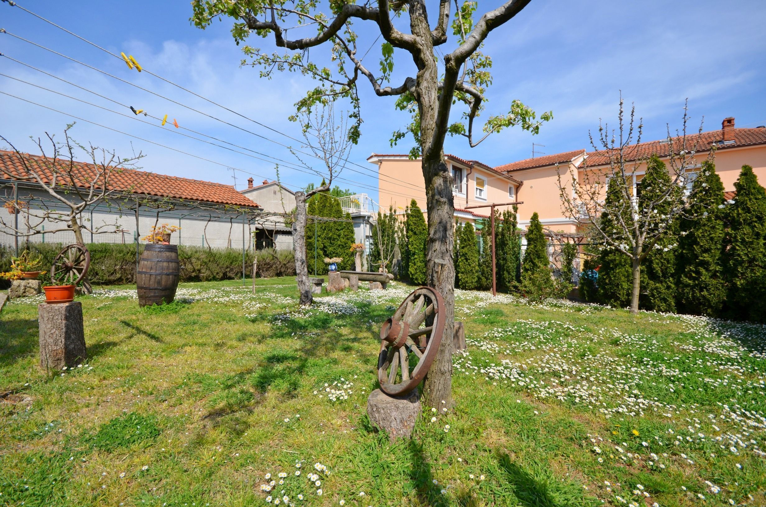 A garden with a wooden wheel, a tree, and a house with a red-tiled roof.