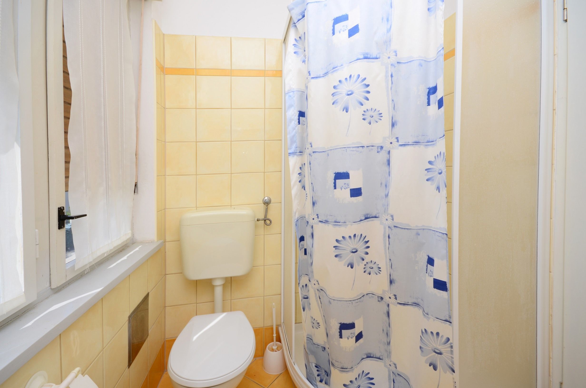 A small bathroom with a toilet, a shower curtain, and a window.