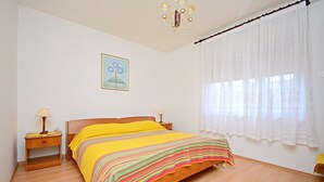 Quarto com cama, mesa de cabeceira, luminária, janela com cortinas e quadro na parede.