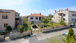 Um bairro residencial com uma casa branca, teto de telhas vermelhas, escadaria que leva a uma varanda e um pequeno jardim.