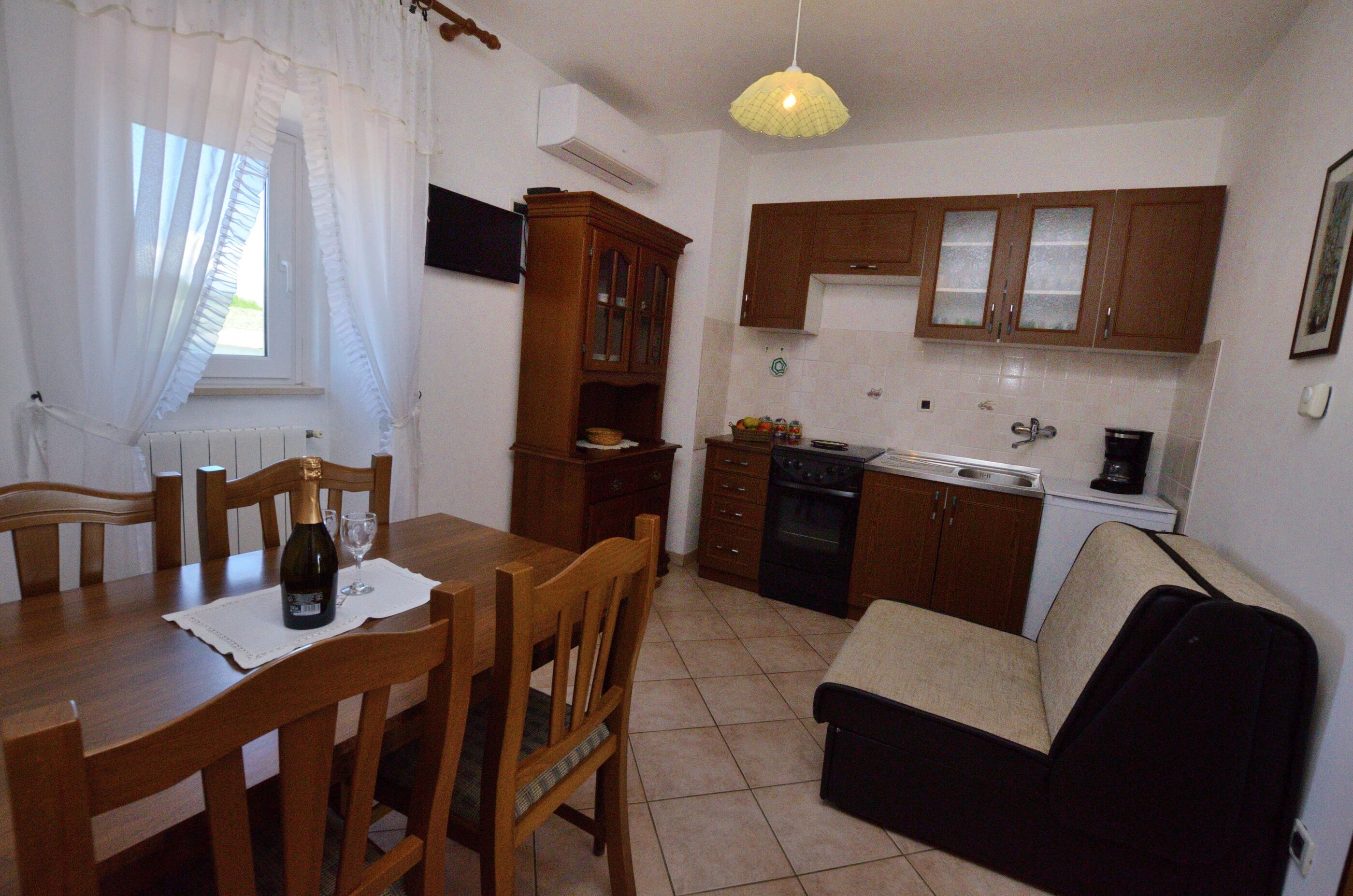 Cocina compacta con armarios de madera, una mesa de comedor con sillas, un sofá y una lámpara colgante.