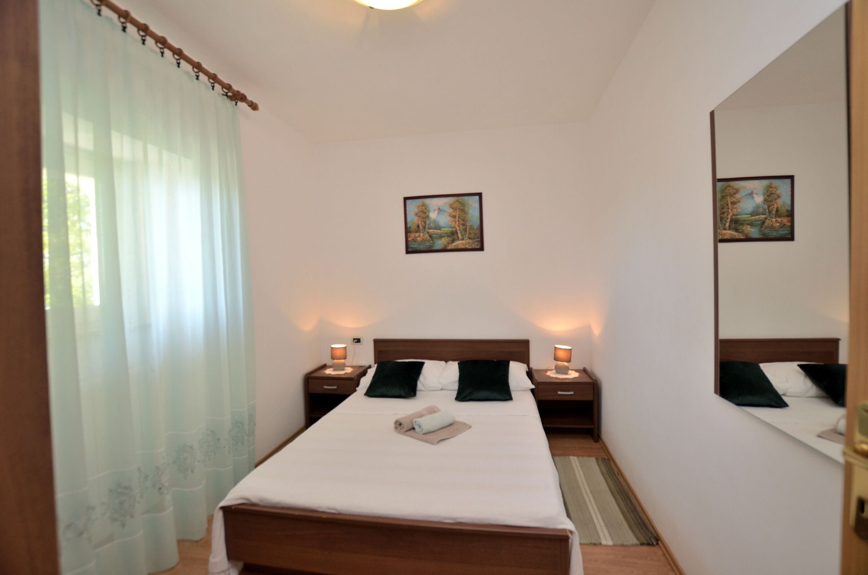 A neatly arranged bedroom with a bed, two bedside tables, a mirror, and two wall-mounted paintings.