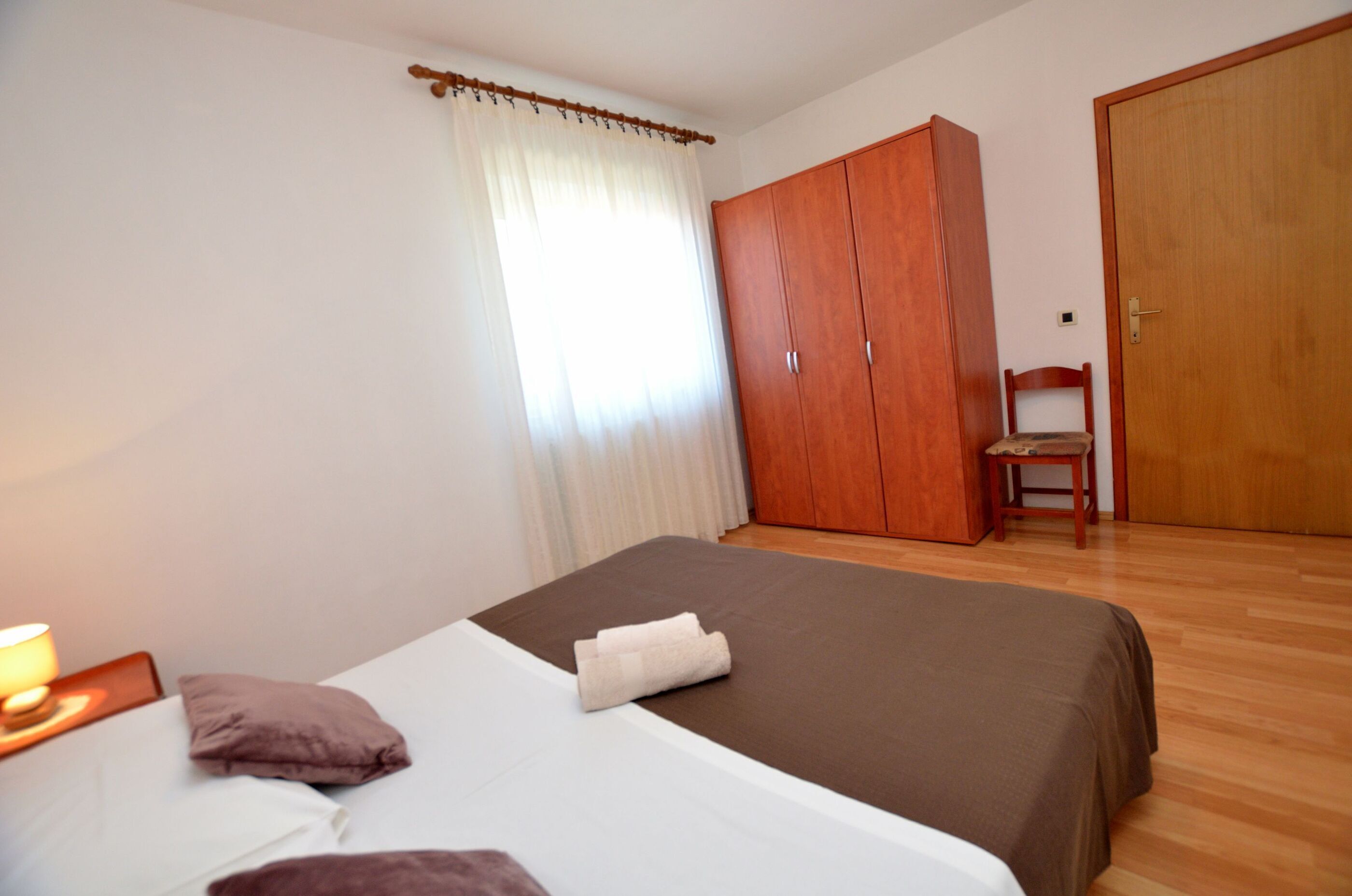 A bedroom with a bed, a wooden wardrobe, a chair, and a window with curtains.