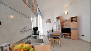 Cocina compacta con pileta, comedor con mesa y sillas, y un pequeño armario con estantes.
