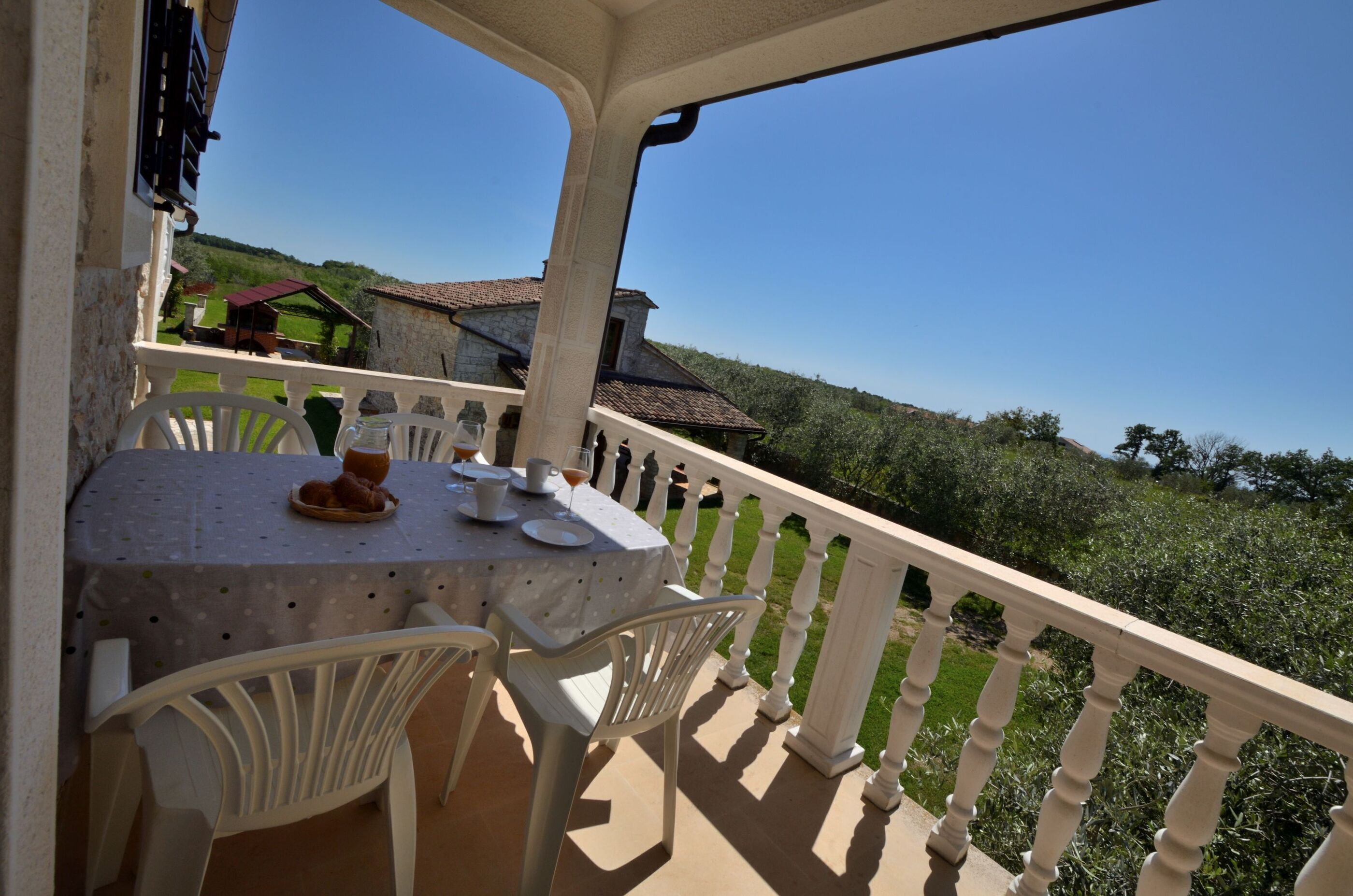 Un balcone con un tavolo apparecchiato per due, affacciato su un paesaggio verde.