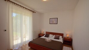 Un dormitorio con cama de madera, cortinas blancas, un cuadro en la pared y lámparas de noche.