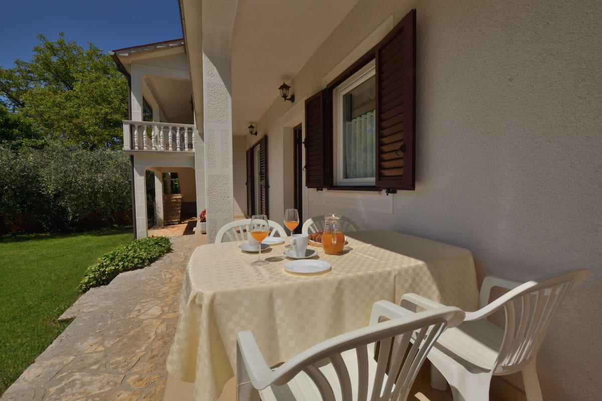 An outdoor dining area with a table set for two, white chairs, and a glass pitcher of orange juice.