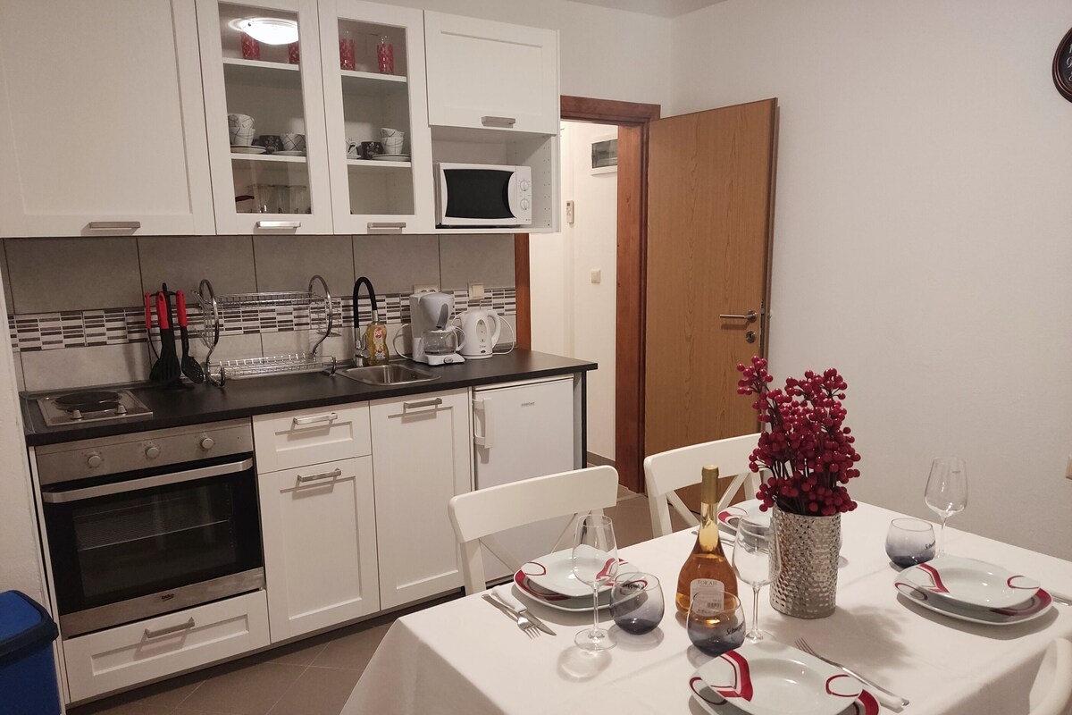 A modern kitchen with white cabinets, a microwave, and a coffee maker. There is a dining table set with plates, glasses, and a vase of flowers.