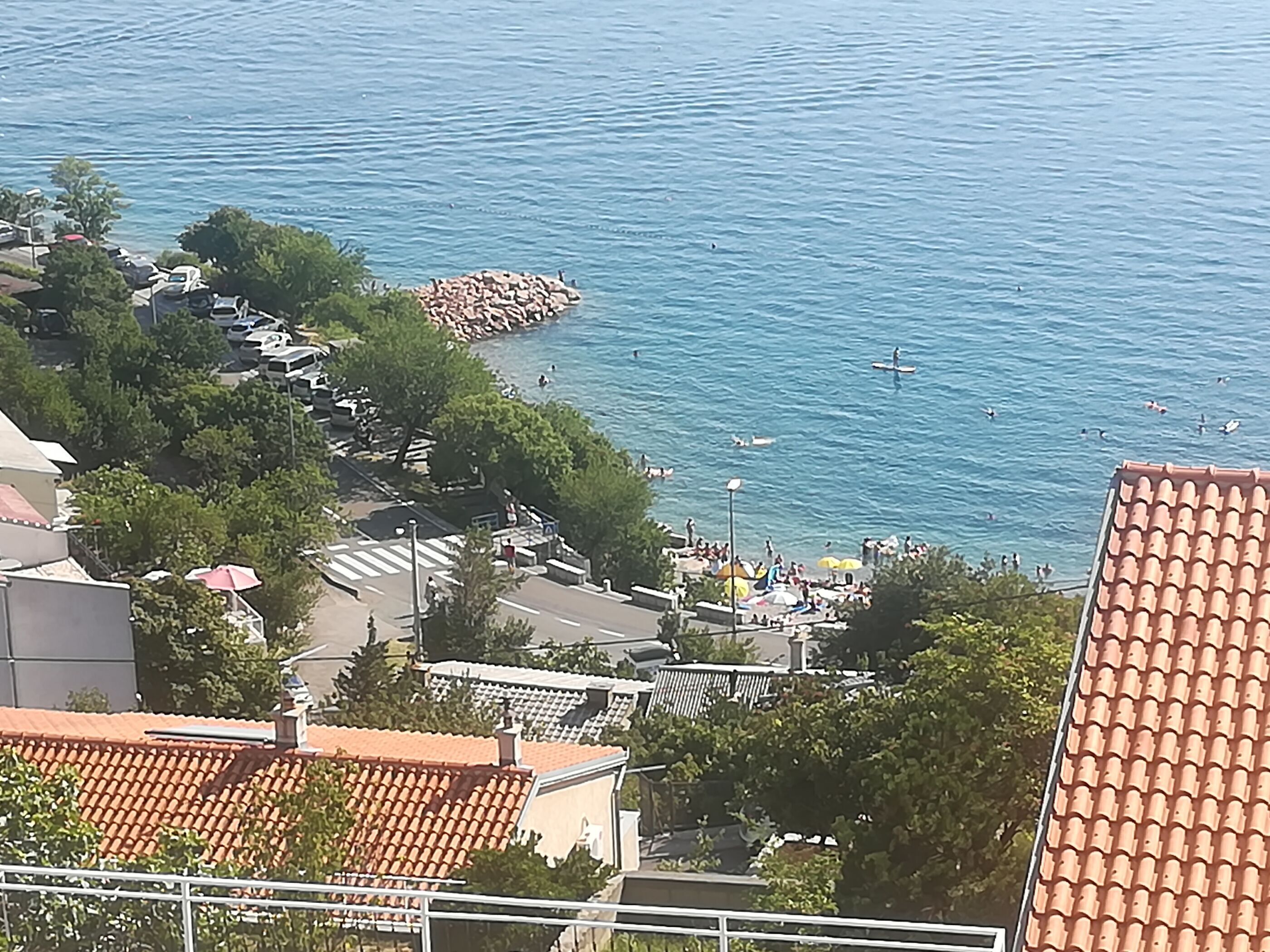 Une zone résidentielle côtière avec des maisons, une digue rocheuse et une plage où les gens se baignent et prennent des bains de soleil.