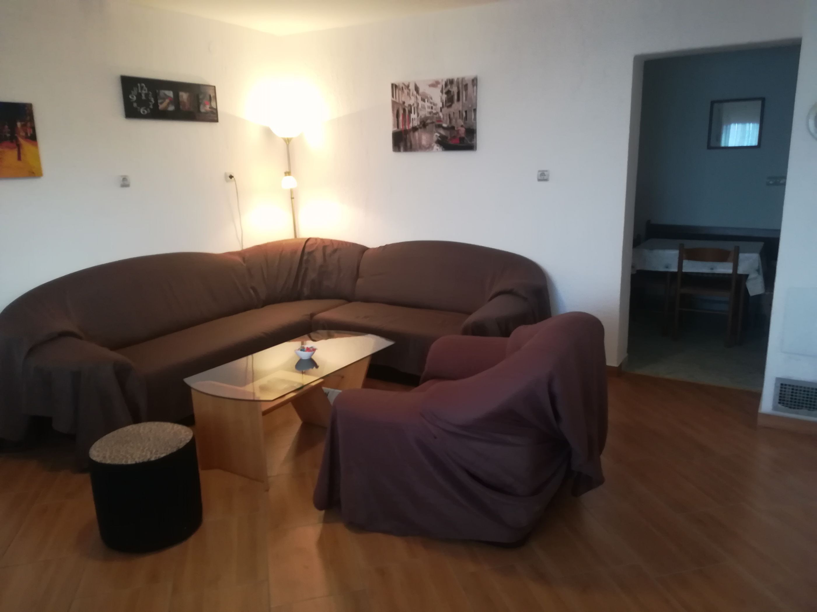 A living room with a curved brown sofa, a small round ottoman, a glass coffee table, and a purple armchair.