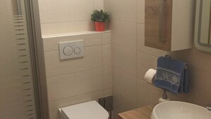 Pieni kylpyhuone, jossa on wc, pesuallas ja suihku.