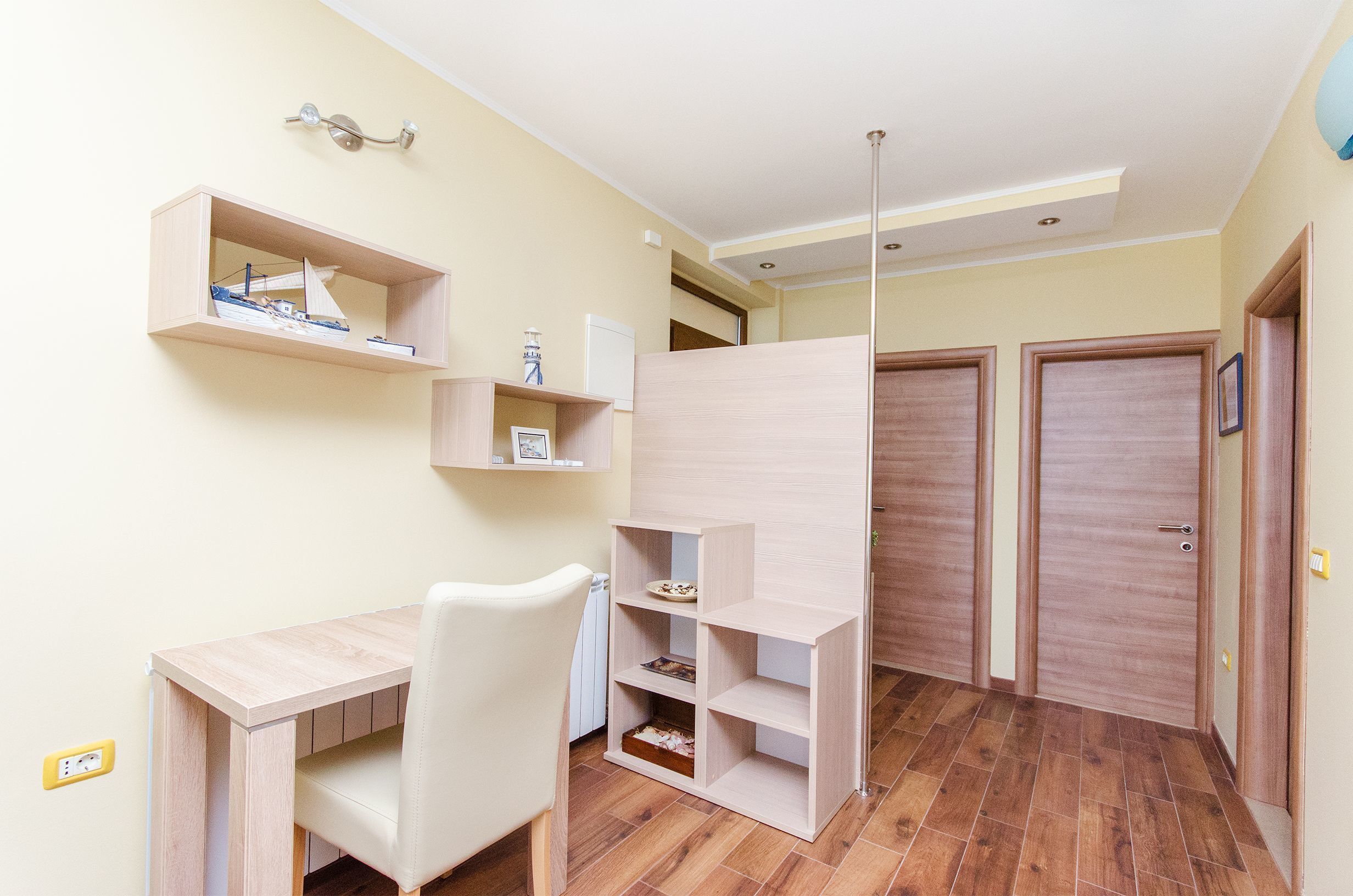 A room with a wooden desk, a chair, a shelf with a model ship, and two wooden doors.